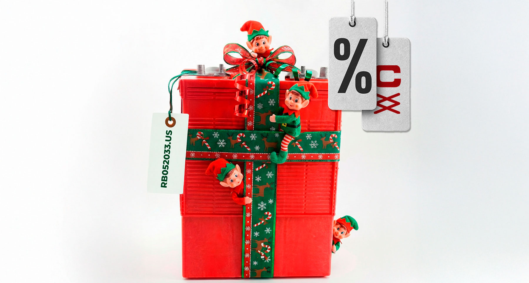 Batería roja envuelta como regalo navideño con elfos traviesos alrededor y etiquetas de descuento de RB Componentes.